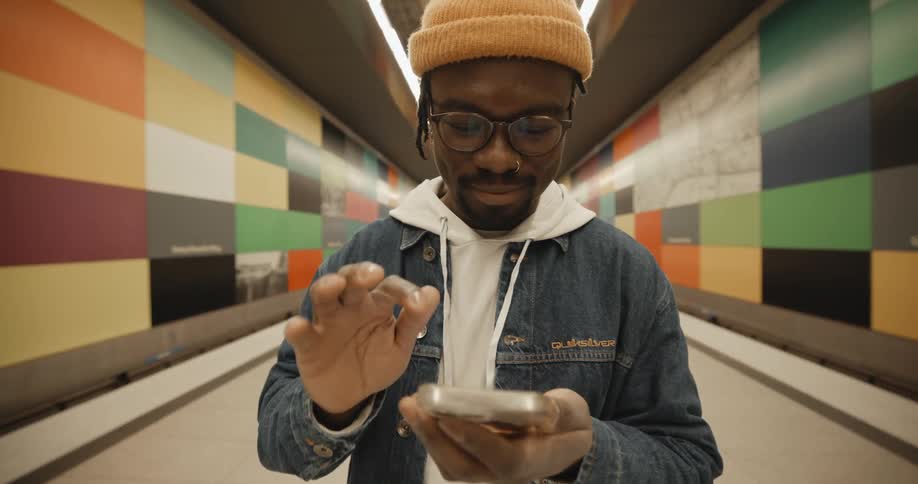A man standing alone on a train station platform holding his phone and tapping the screen