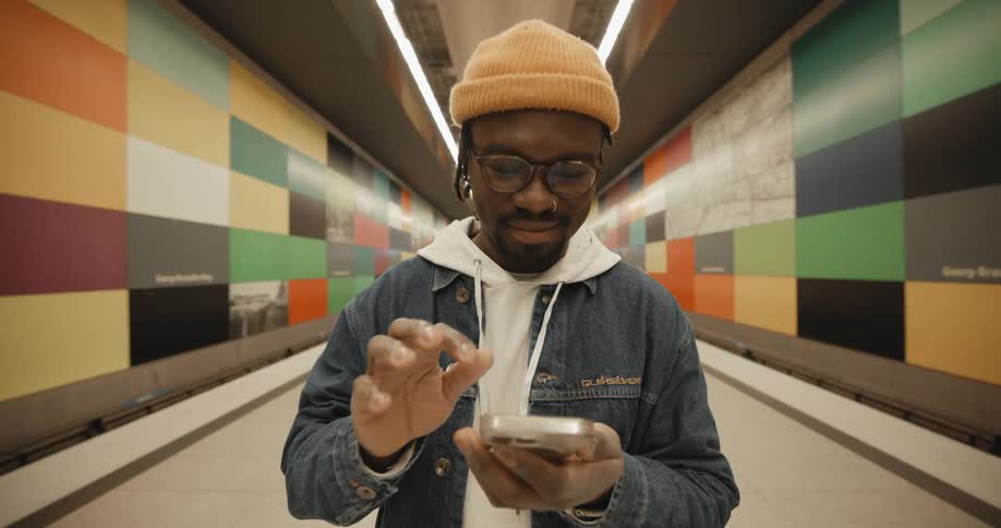 A man texts on his phone while standing in a hallway