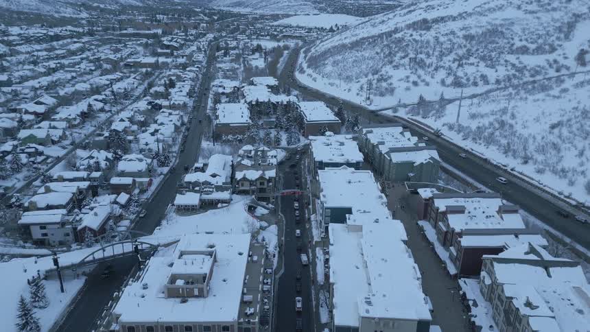 An aerial view of snow covered houses and stores with people walking on sidewalks and cars driving