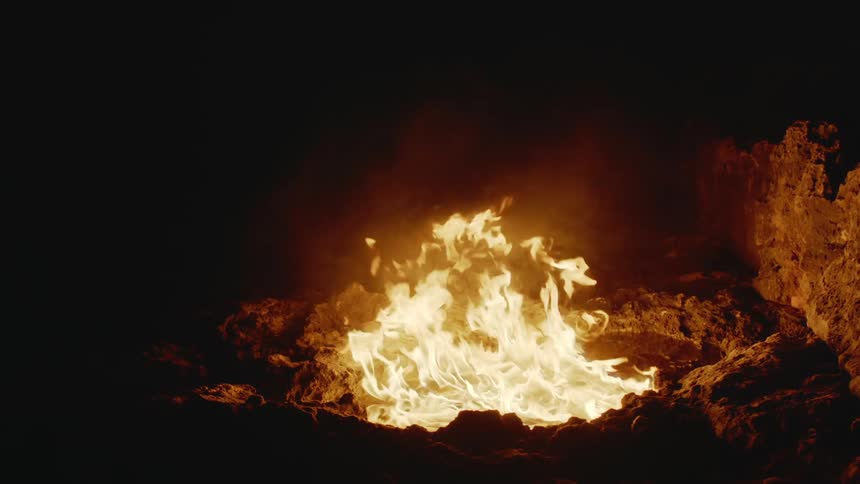 The bright flames of a bonfire are moving as they burn and smoke rises from the blaze in the darkness