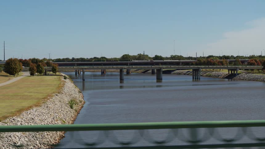 Automobiles travel on a bridge across a river under a clear sky