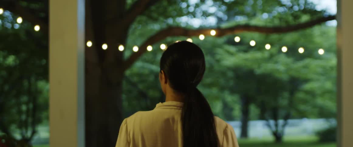 Woman walking through a doorway to the outdoors and take her hair out of a pony holder