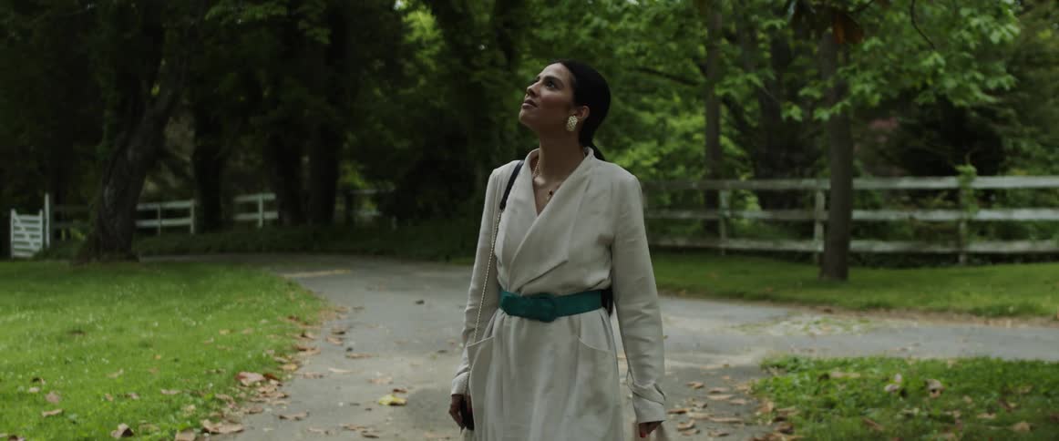 A woman wearing a white dress walks and then spins on a walkway under trees