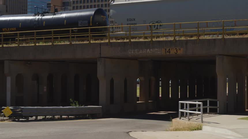 Traffic moves under bridge with stopped train near downtown skyscrapers