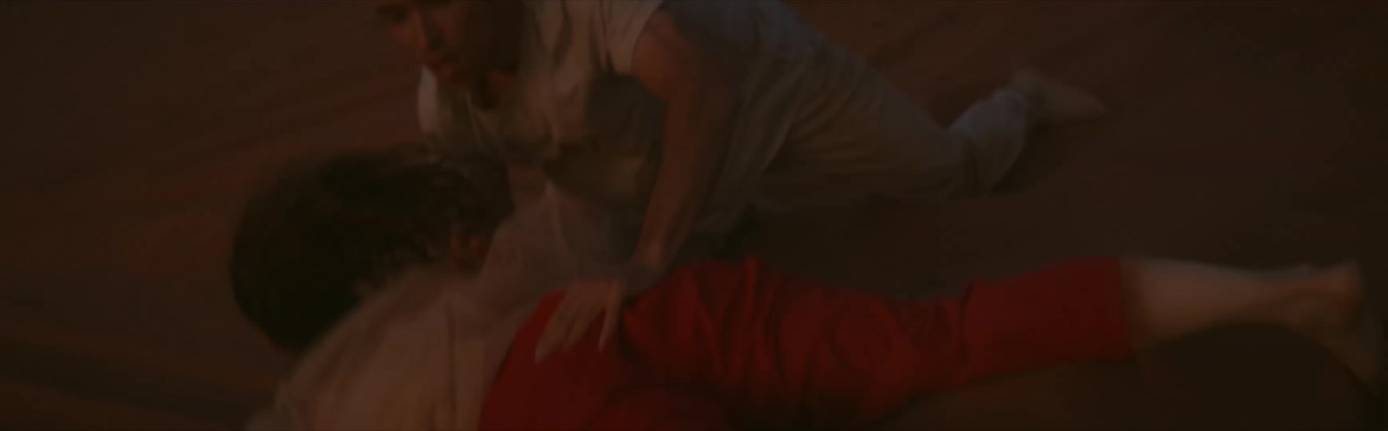 A man and a woman are on the ground in the desert and he is rolling her across the sand