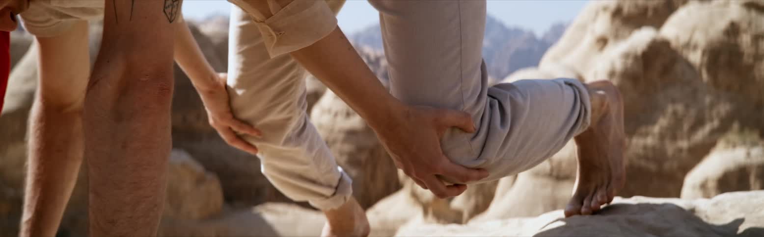 A man and woman crab walk along rocks in a canyon