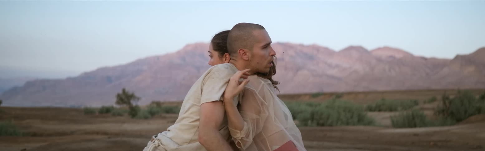 A woman stumbles backwards and pushes a man that is falling against her and pushing her across the landscape