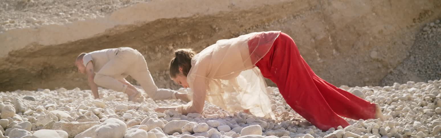 A couple struggling to advance against the wind over a rocky terrain in the deser