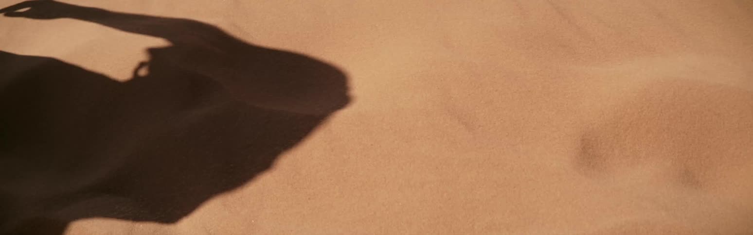 Shadow of person moves across sand