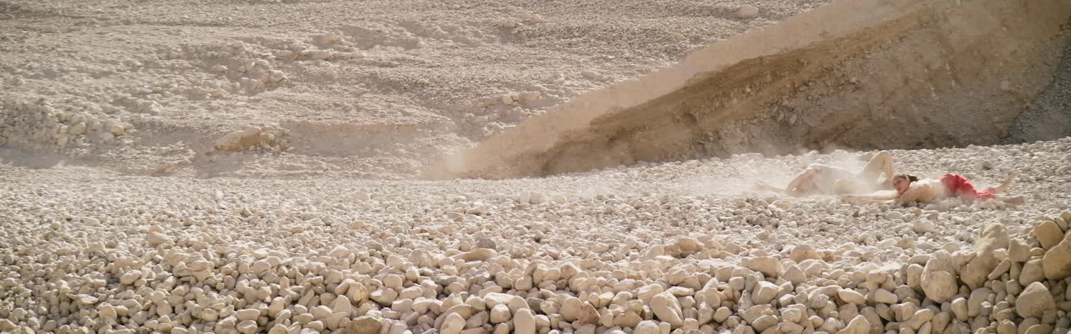 A man and a woman lying on the ground are mysteriously being pulled across rocks in the desert by an unknown force they cannot resist or stop