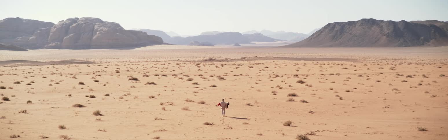 A person carrying another person walking through the sandy desert toward a canyon