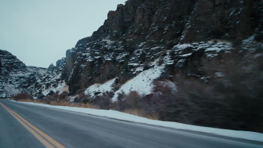Mountains with light snow cover are along the roadside among plants and vegetation on a winter day
