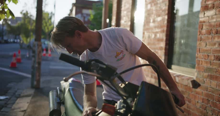 A man tries to start his motorcycle while parked on a sidewalk