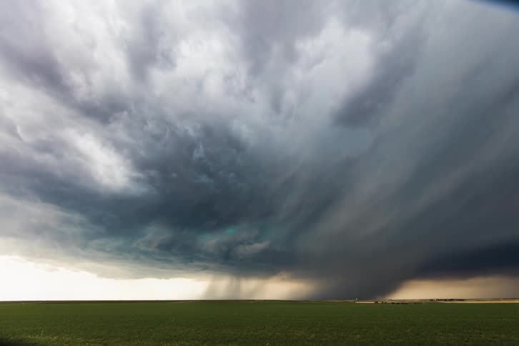 Wide landscape of farmland or prairie with dark storm clouds coming in and possible tornado forming