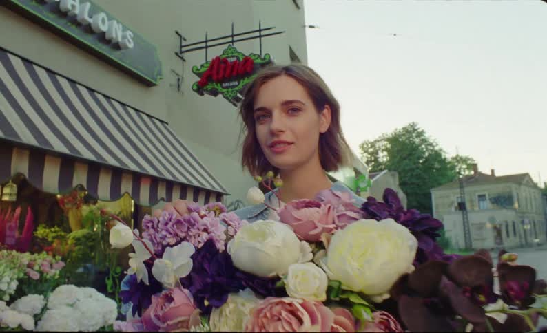 Young woman standing outside of florist shop holding touching and admiring a huge bouquet of purple lavender white and pink flowers