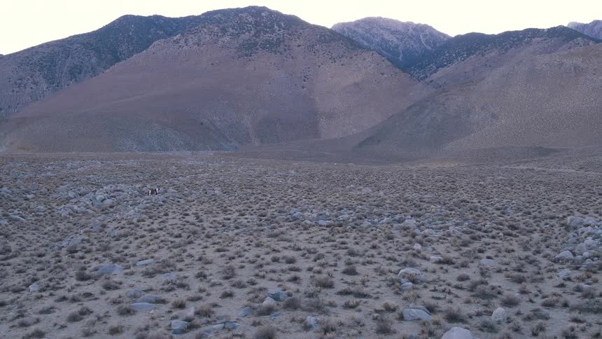 A man and horse crossing land at the base of a mountain range