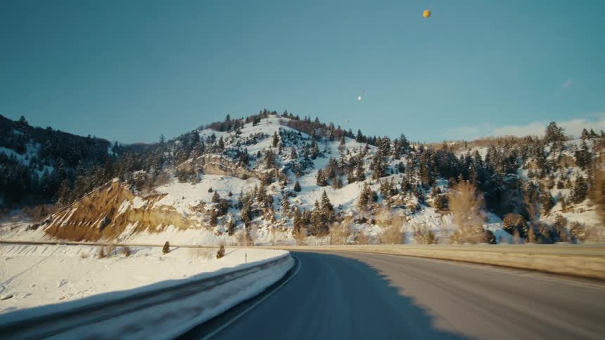 Small balls hover near forested mountains in winter near highway