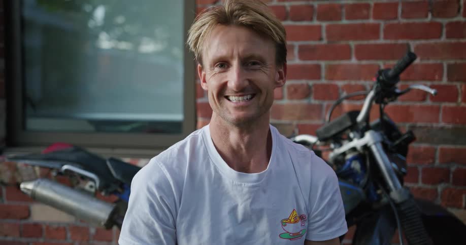 A man is standing outdoors and is smiling