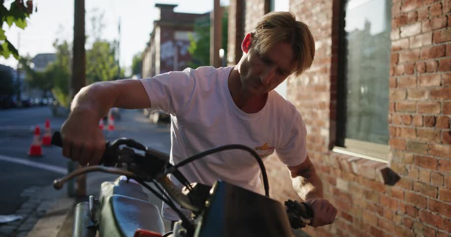 Man sitting on stationary motorcycle on sidewalk starting engine and revving throttle with right hand