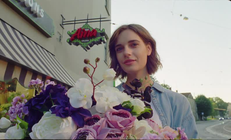 Woman with brown hair and denim shirt holds a bunch of flowers and smiles at camera