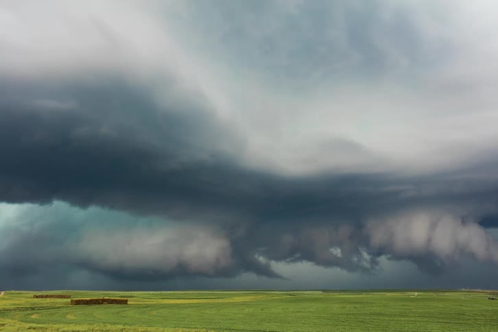 Dark supercell storm clouds gather over green field