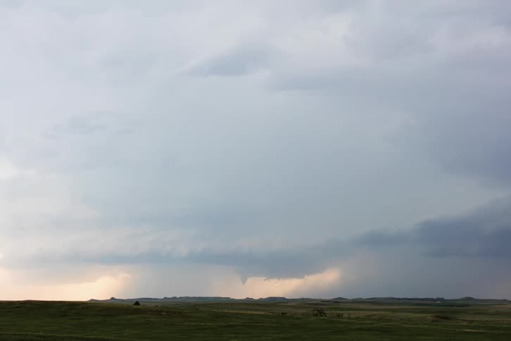 A distant tornado forms and moves across the landscape