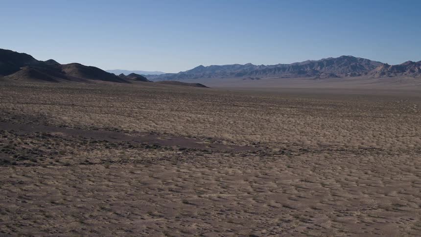 A vast desert plain leads to hills under a blue sky