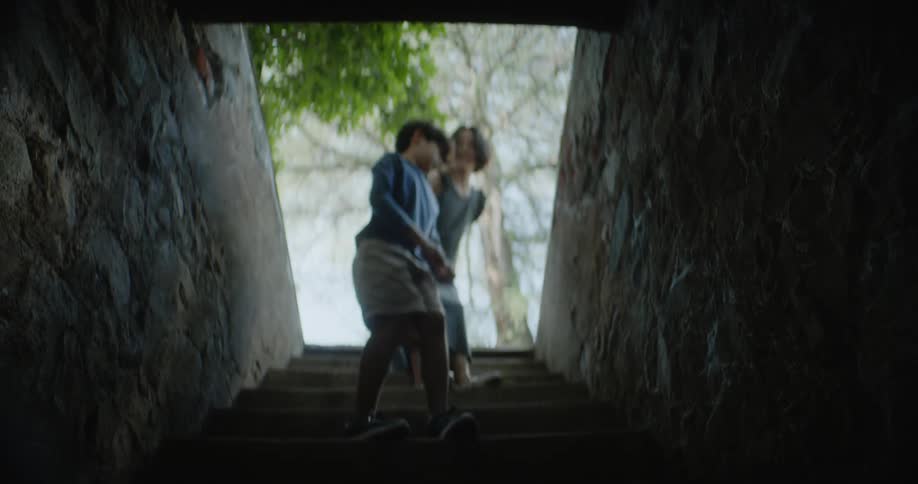A mother leads her son up the dark stairwell