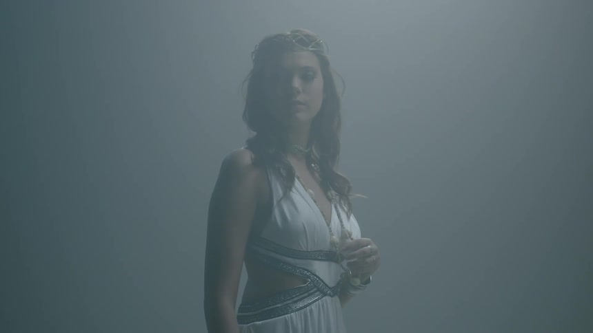 A woman in a while dress looks around and holds her necklace