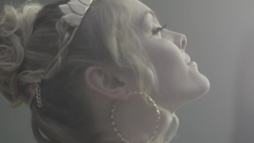 A blond woman wearing earrings looks up toward a light