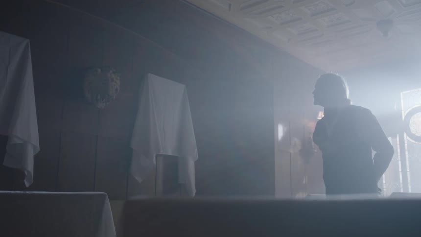 A man walks into a room and puts his arms behind his back