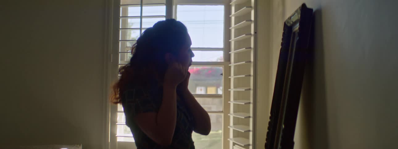A woman puts on earrings while standing in front of a mirror