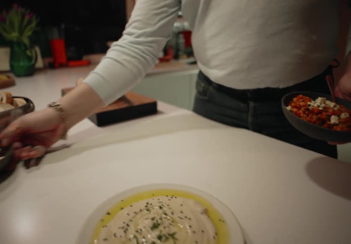 A womans hands are shown picking up two bowls of nuts off the counter after which she walks away