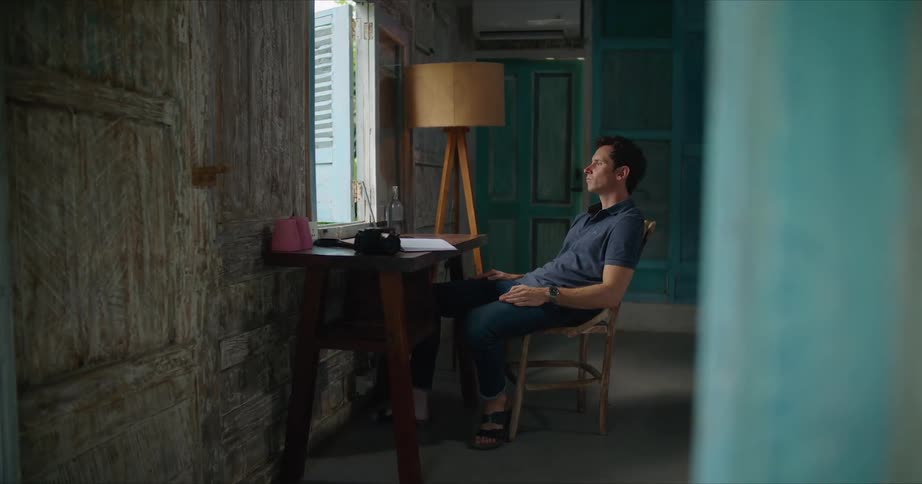 A man sitting at his desk looking out the window contemplatively tapping his hands on his leg