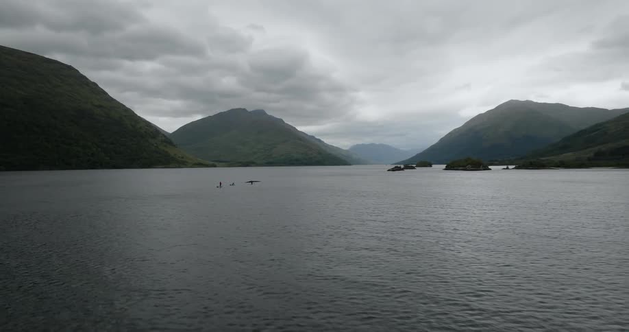 Three paddleboarders crossing a large lake with mountains in the background