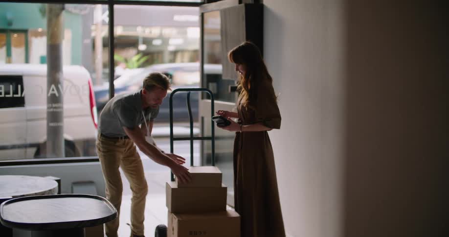 A man is delivering packages to a business as he hands a device to the woman to sign