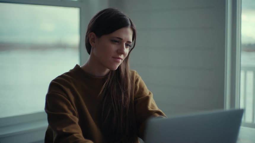A young woman sits at home and uses a laptop