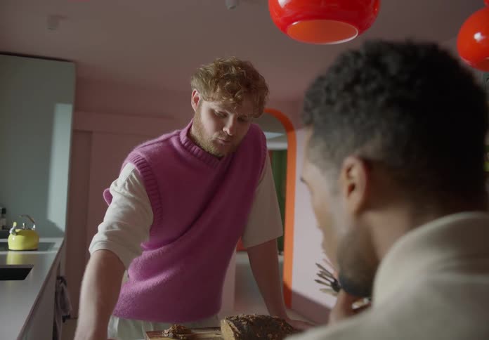 Two men eat bread with jam in their kitchen