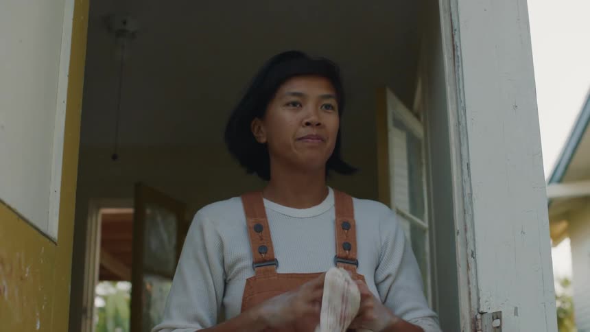 A woman stands in the doorway of her home as she wipes her hands with a towel and walks outside