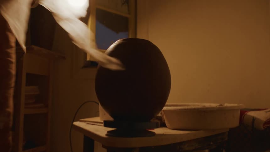 Person pulls thin cloth off clay sculpture in workshop at night