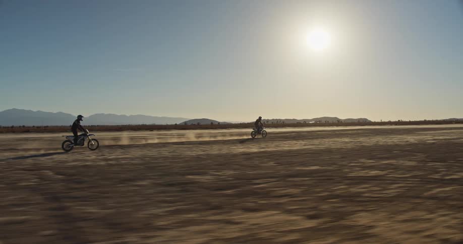 Two people riding dirt bikes in the desert on a sunny clear day