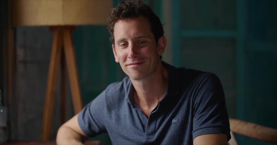 A man smiles while posing on a chair at home