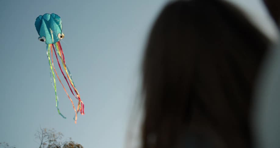 An adult helps a child fly an octopus kite with googly eyes and ribbon tentacles