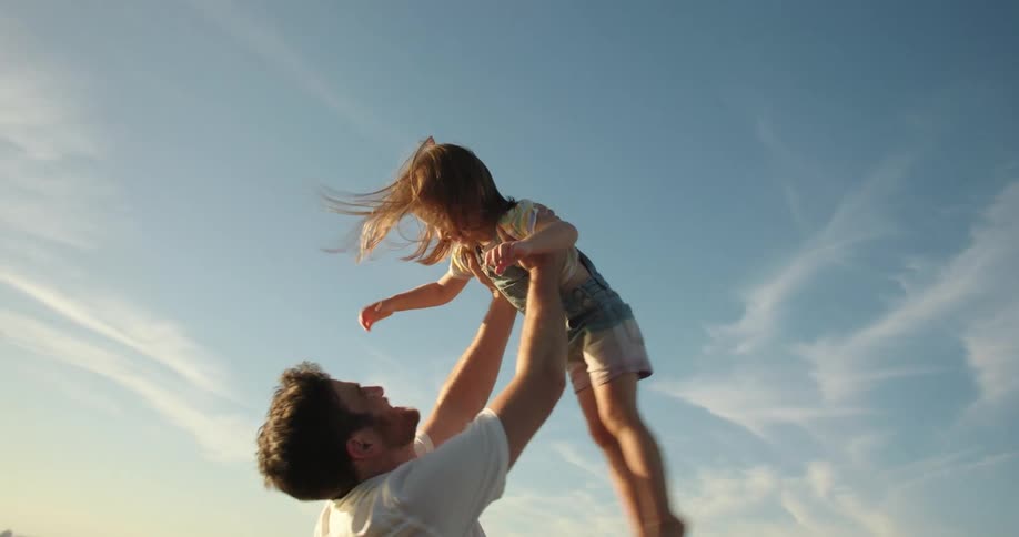 A little girl running into her fathers arms on the beach smiling and laughing