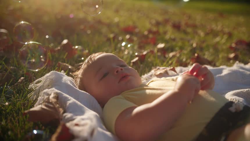 Baby boy laying on a blanket in the grass fallen leaves around him and soap bubbles floating above his head