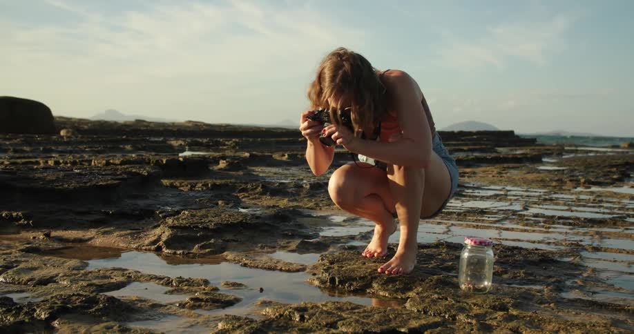Woman with brown hair top and shorts photographs mud in the muddy beach next to the ocean
