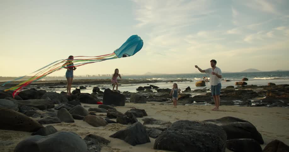 Family plays on beach with kite far from the city skyline in the distance