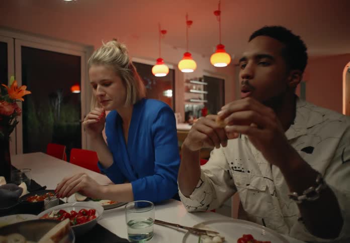 A woman and a man sit at a counter and enjoy a meal while talking and gesturing