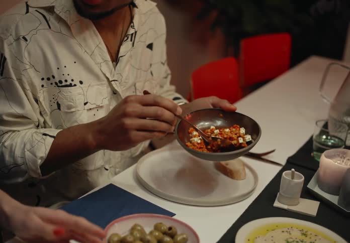 A woman passes a bowl of food to the man sitting beside her who spoons for of the contents onto his plate