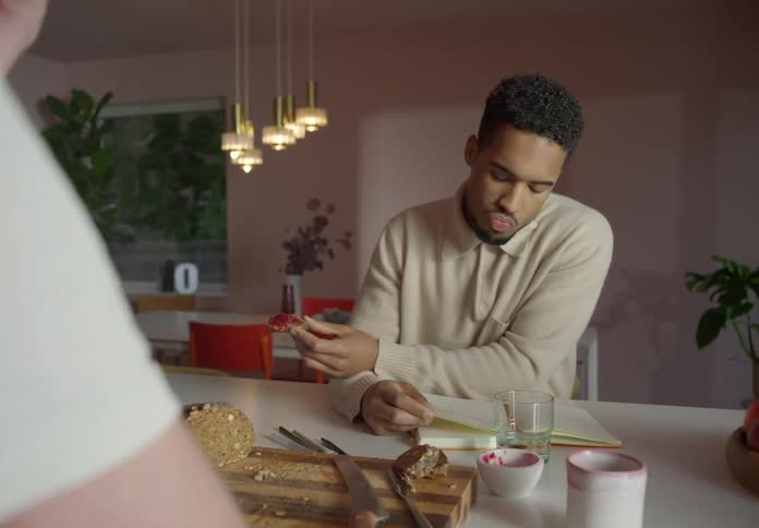 Man eats and reads across counter from another person in home